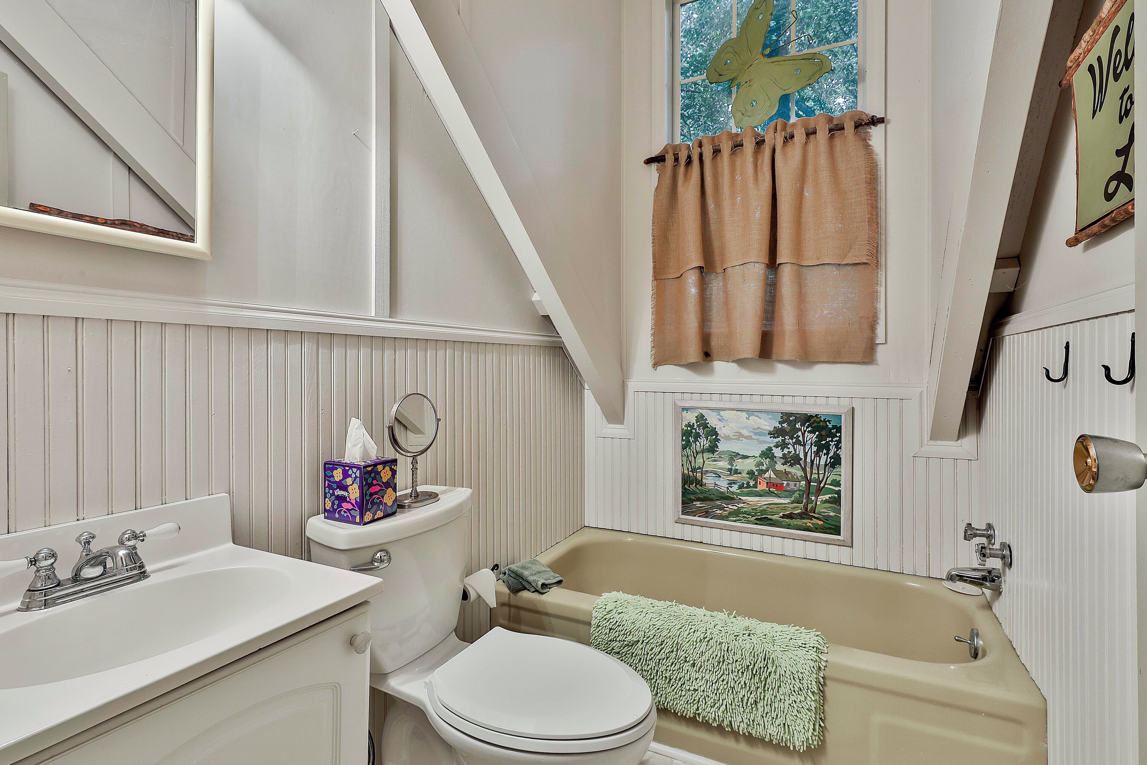A bathroom with a sink, toilet, bathtub, and a painting on the wall.