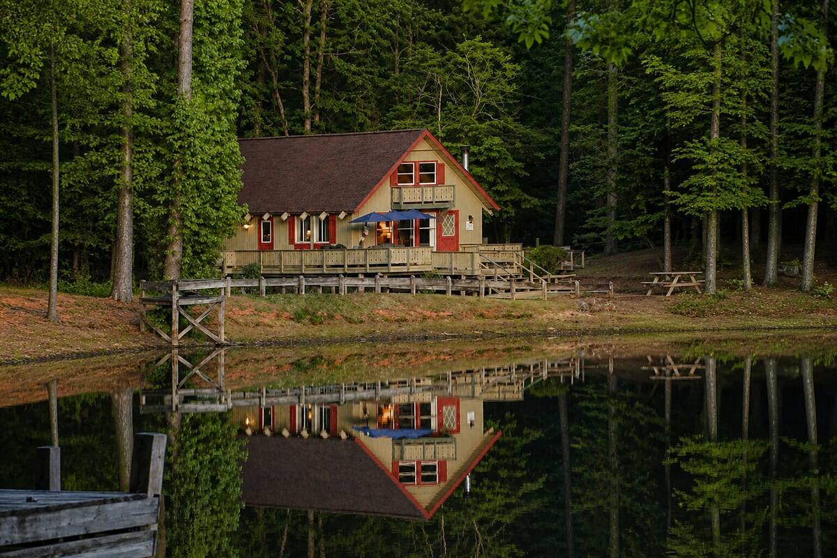 A cabin with a deck, a dock, and a reflection in the water.