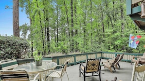 A wooden deck with a glass table and chairs, surrounded by lush greenery. - Pine Mountain Club Chalets Resort (Pine Mountain)