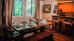 A dining area with a wooden table set for four, a bench, and a kitchen in the background. - Pine Mountain Club Chalets Resort (Pine Mountain)