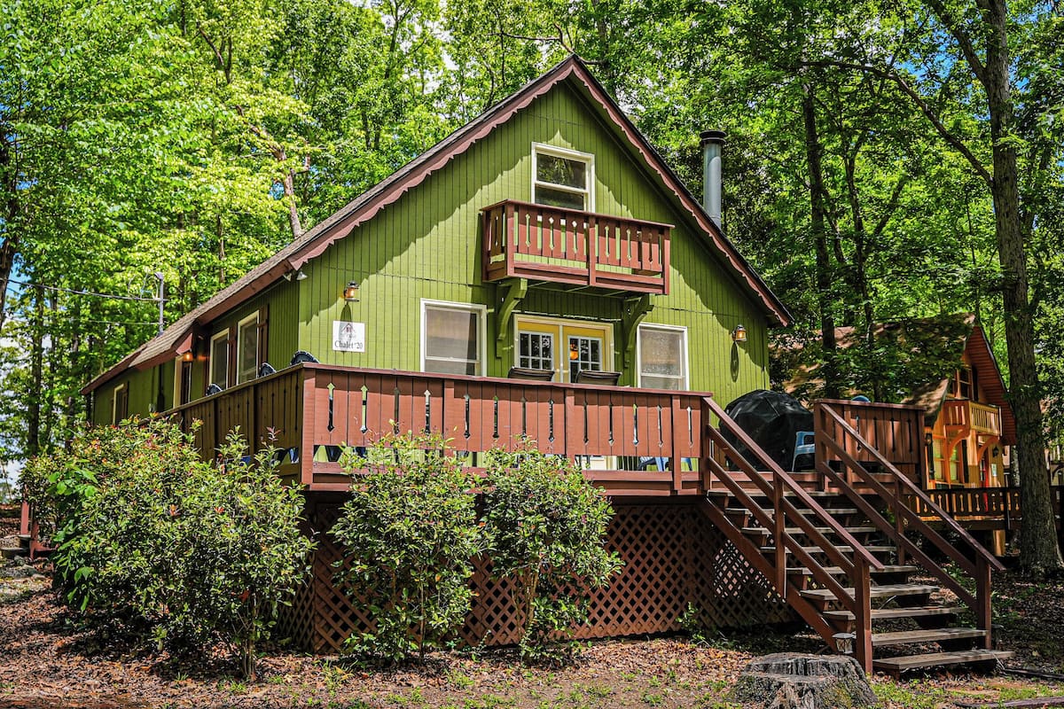 A green cabin with a balcony, wooden deck, and a staircase leading to the entrance.