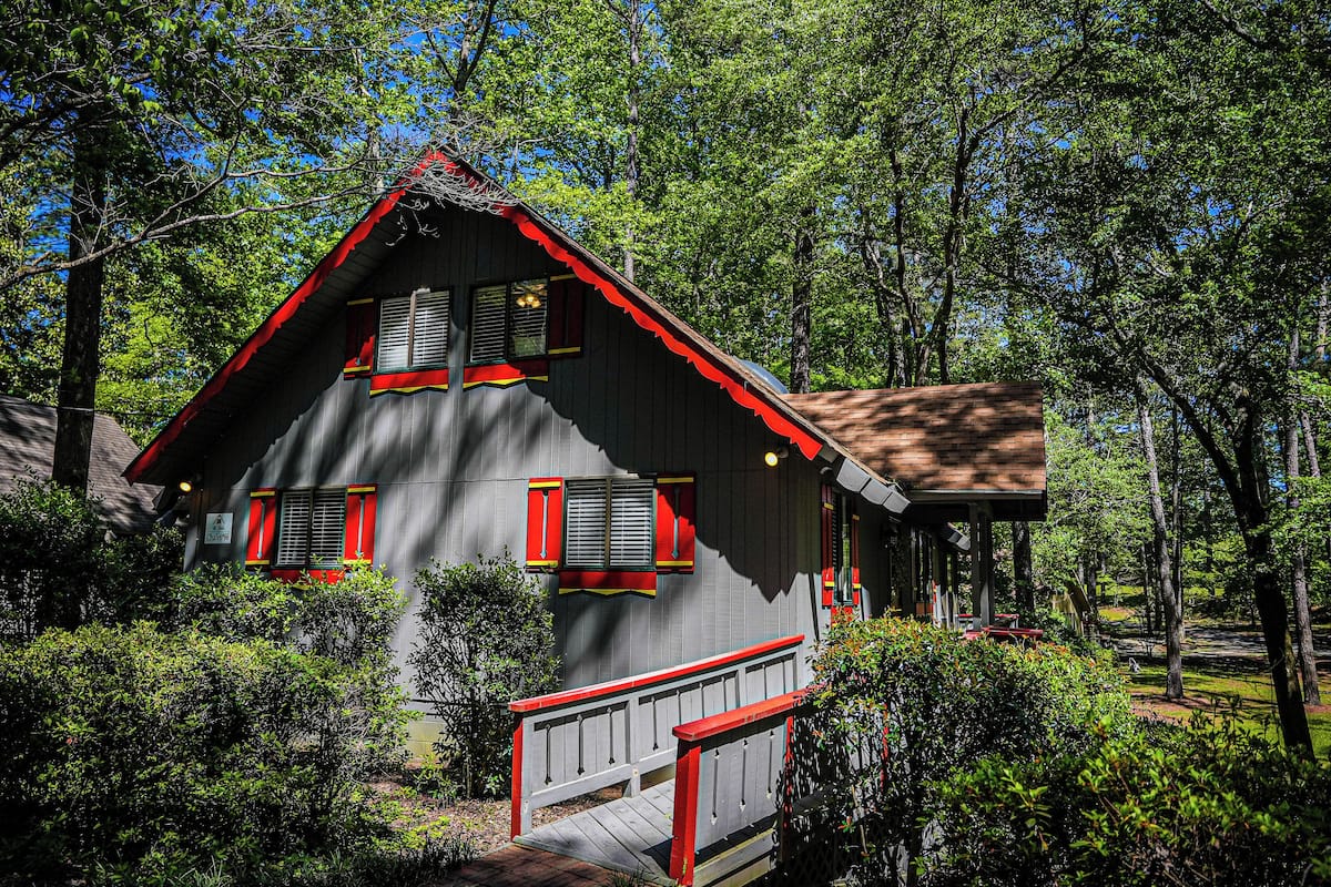 A cabin with a red roof, white trim, and a wooden deck.