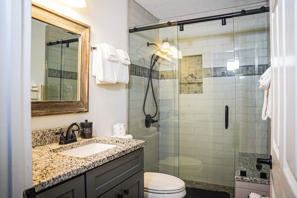 A bathroom with a glass-enclosed shower, a sink with a granite countertop, and a mirror above the sink.