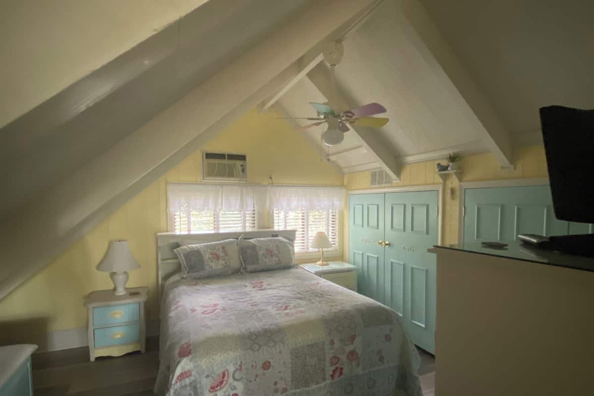 A bedroom with a bed, a nightstand, a dresser, a ceiling fan, and a window with blinds.