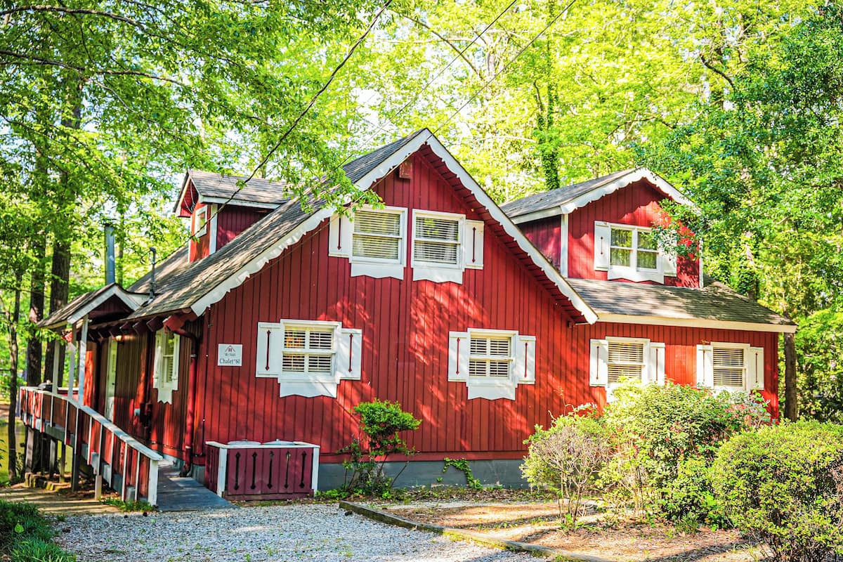 A red wooden house with a porch, a small garden, and a gravel path.