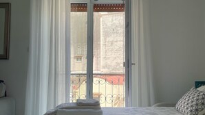 A hotel room with a bed, a window with white curtains, a view of a balcony, and a door leading outside. - La Corte Dei Naviganti B&B - Amalfi Coast - Cetara (Cetara)