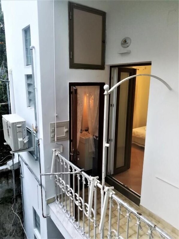 A balcony with a white railing, a door leading to a room with a bed, and a small window. - La Corte Dei Naviganti B&B - Amalfi Coast - Cetara (Cetara)