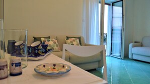 A living room with a sofa, a dining table with plates and cups, and a view of the outside through a glass door. - La Corte Dei Naviganti B&B - Amalfi Coast - Cetara (Cetara)