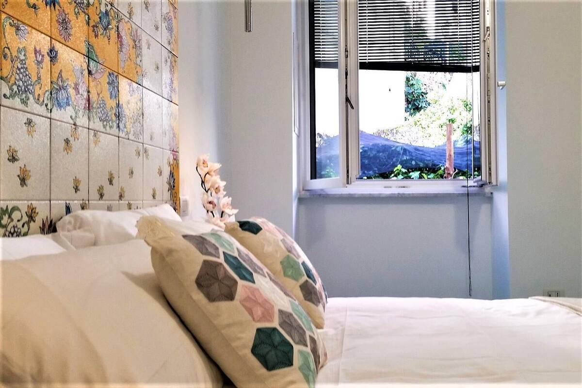 Un dormitorio con cama, ventana con persianas y pared de azulejos con motivos florales.