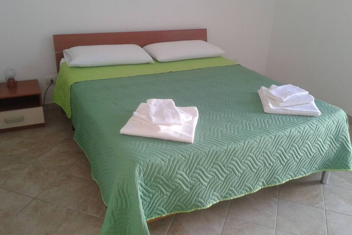 Un lit bien fait, avec une couette verte et deux serviettes blanches pliées posées sur le lit.
