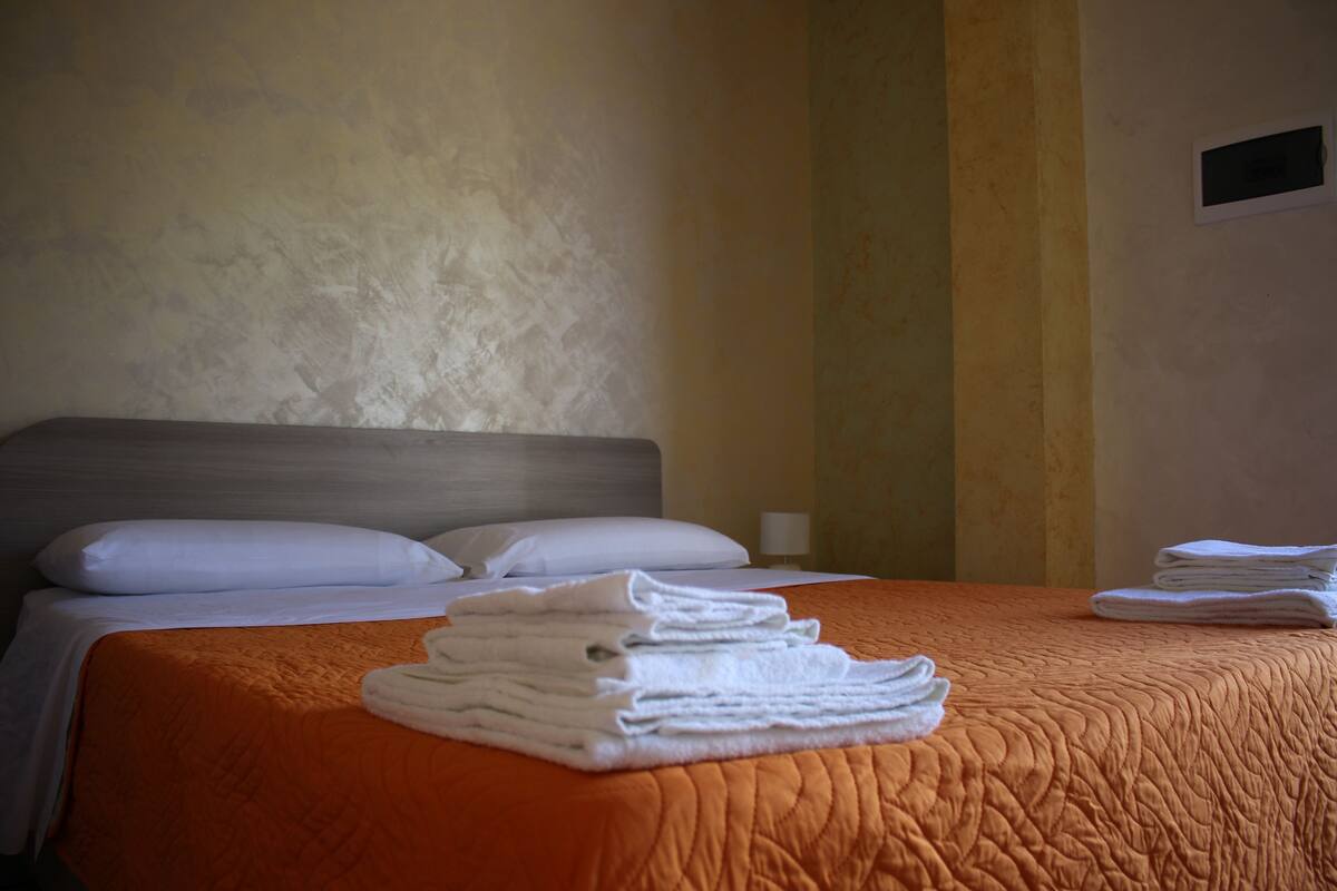 Une chambre d’hôtel avec un lit soigneusement fait, une pile de serviettes pliées et un luminaire fixé au mur.