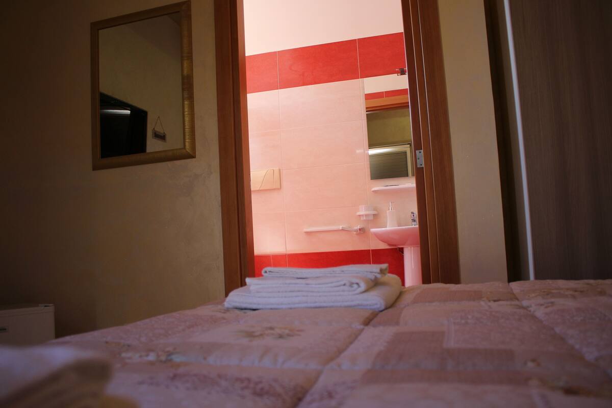 Une chambre d’hôtel avec un lit, un miroir et une salle de bain visible à travers une porte ouverte.