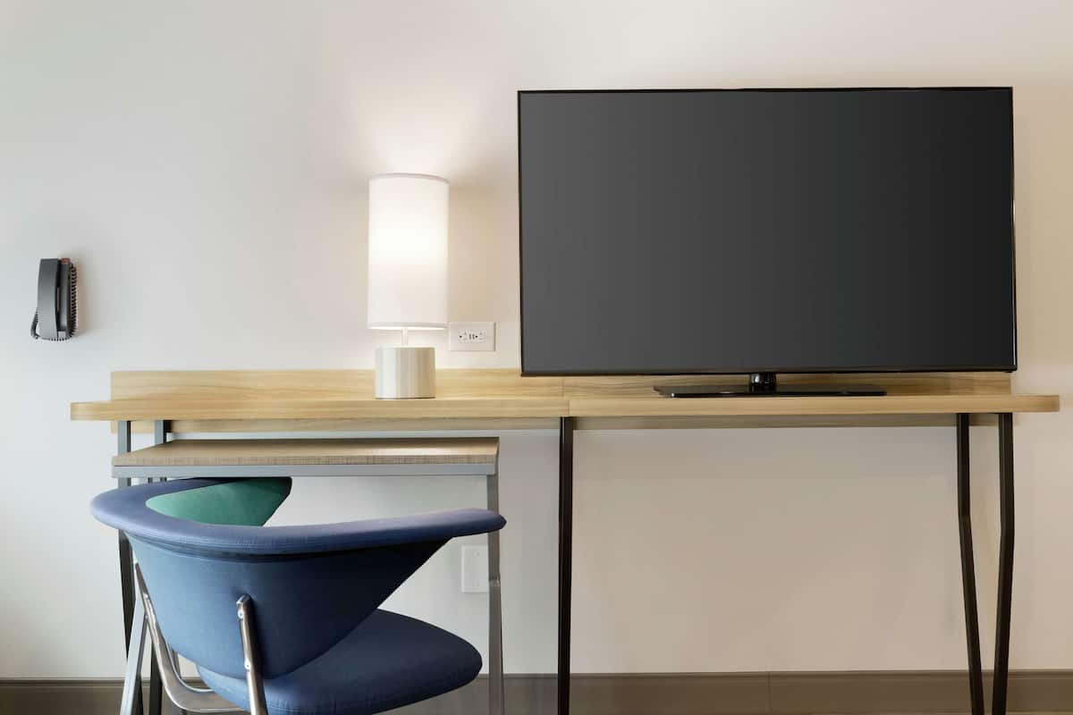 A modern room with a wooden desk, a flat-screen TV, a lamp, and a blue chair.