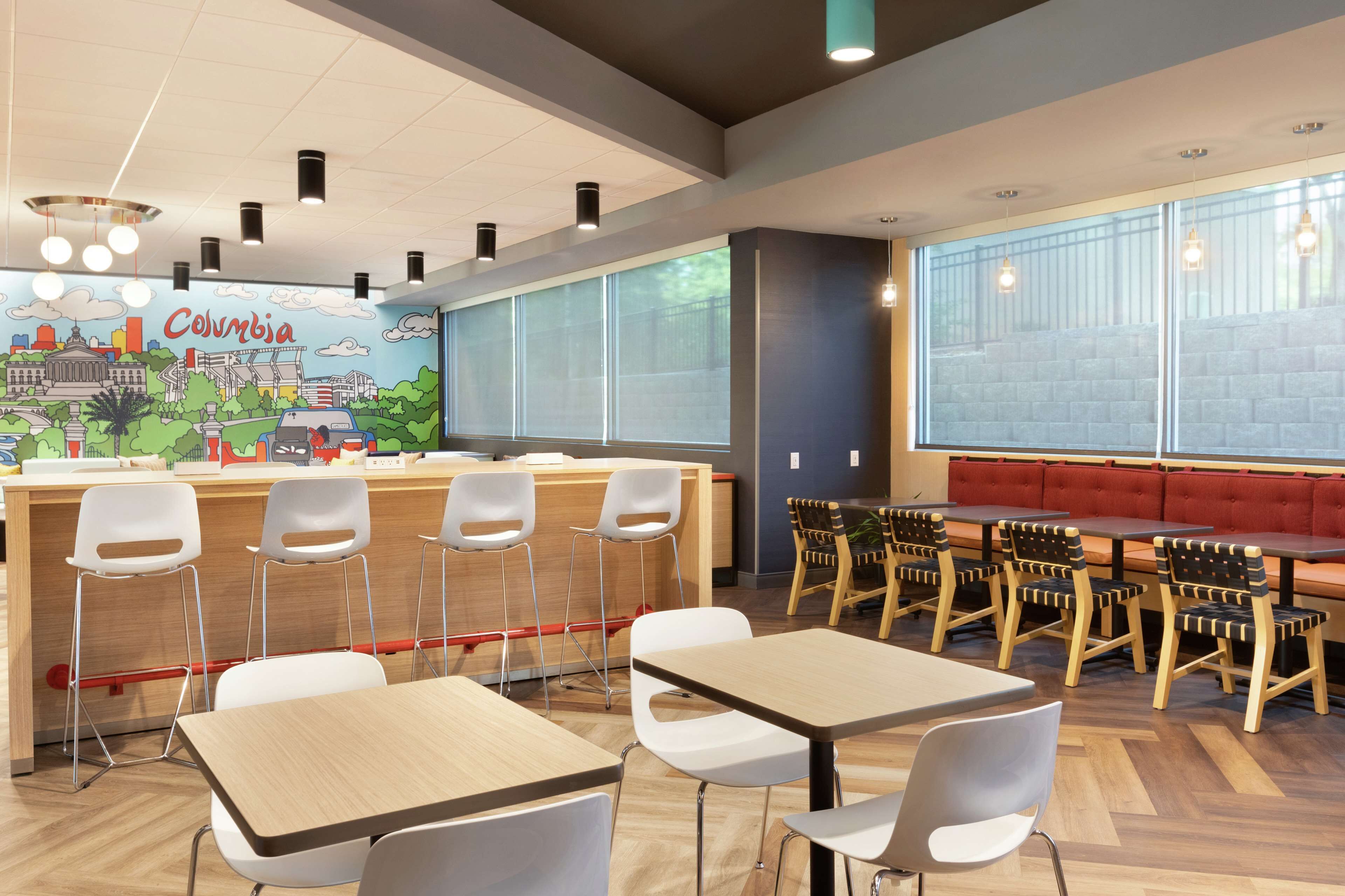 A modern cafe with a mural of Columbia, wooden tables and chairs, and large windows.