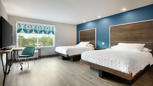 Quarto de hotel moderno com duas camas, uma mesa, uma cadeira e uma janela grande com vista para árvores.
