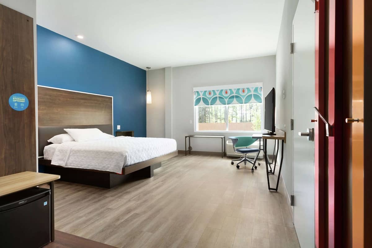 A modern hotel room with a bed, desk, chair, and a window with a view.