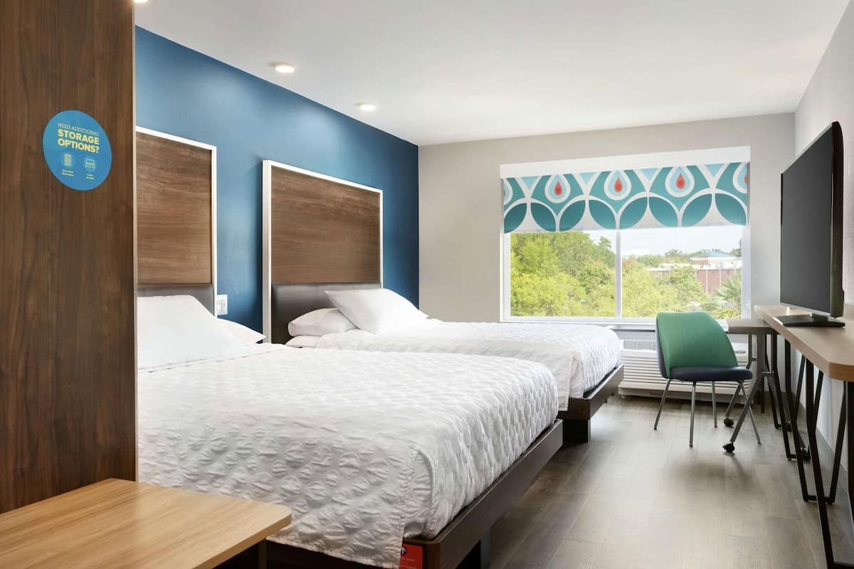 A hotel room with two beds, a desk, a chair, a TV, and a window with a view.