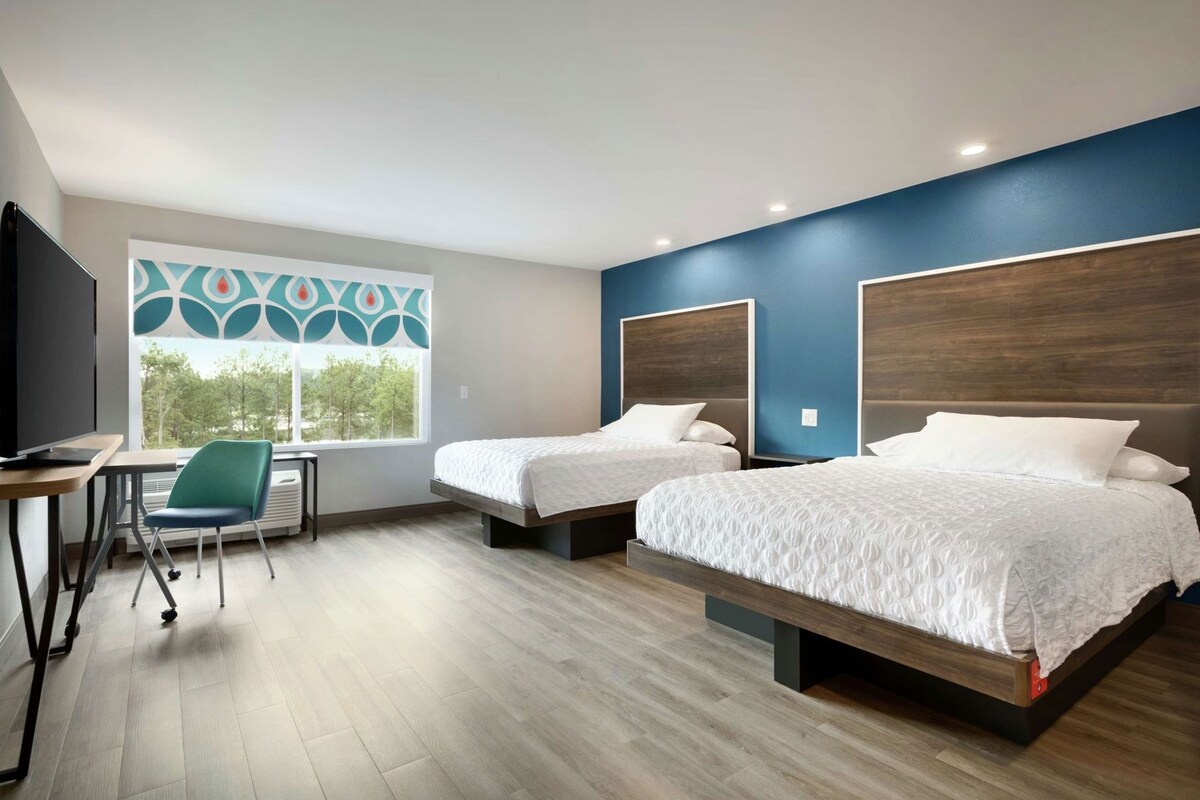 A hotel room with two beds, a desk, a chair, and a window with a view.