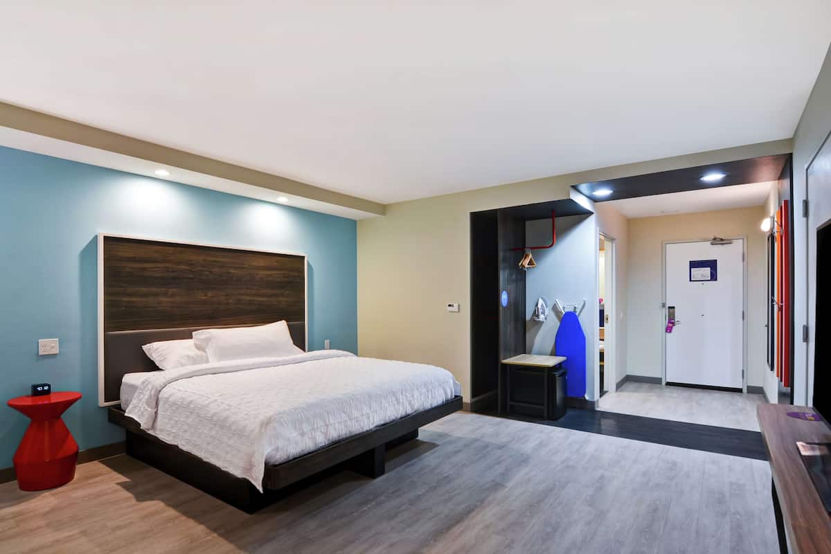 A modern hotel room with a bed, a red side table, and a door leading to a bathroom.