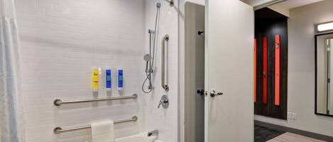 Une salle de bain moderne dotée d’une douche à l’italienne, de barres d’appui et d’une baignoire.