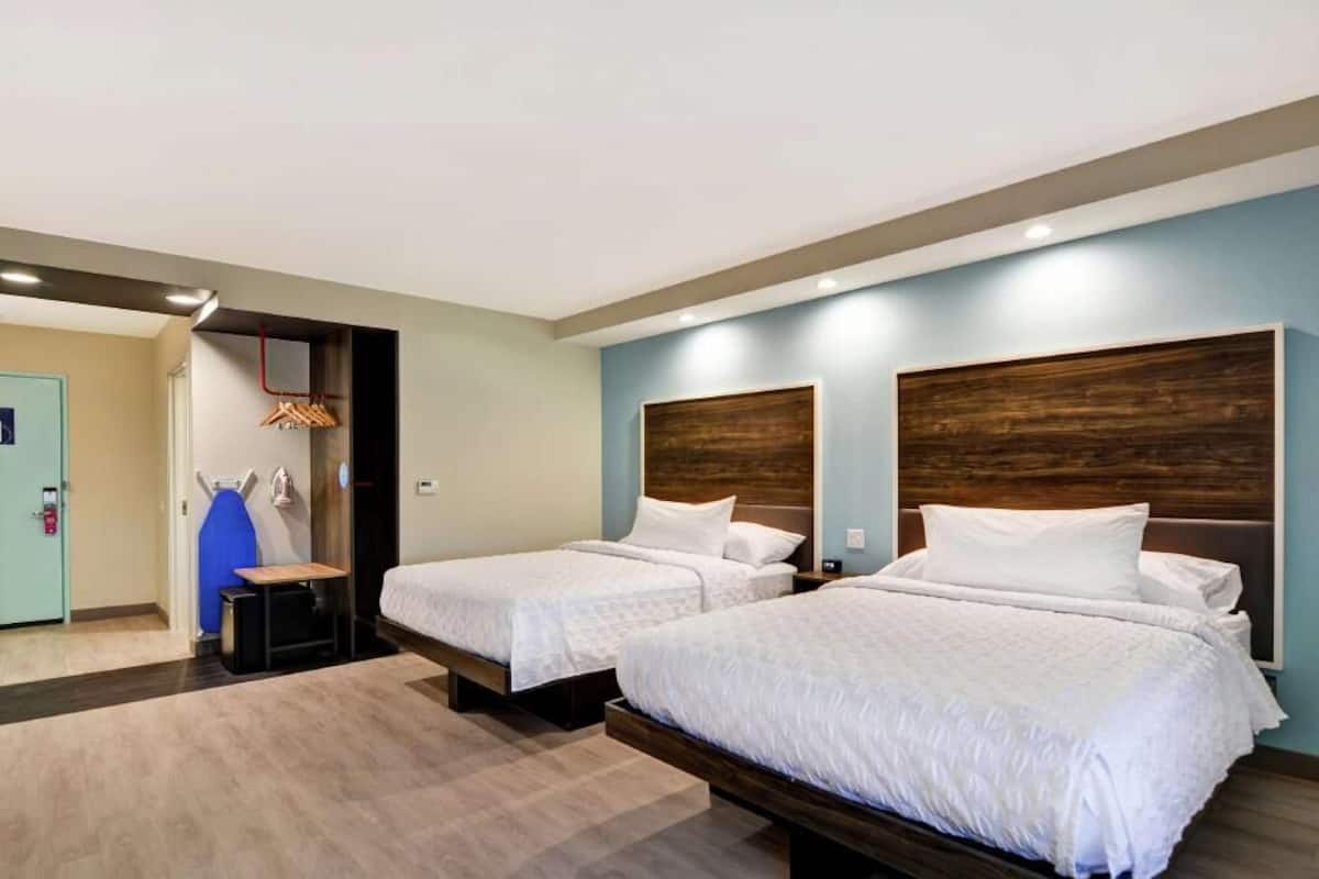 A hotel room with two beds, a wooden headboard, a small table, and a blue chair.