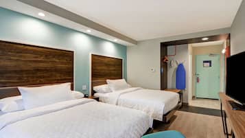 A hotel room with two beds, a television, a desk, and a door leading to a hallway.