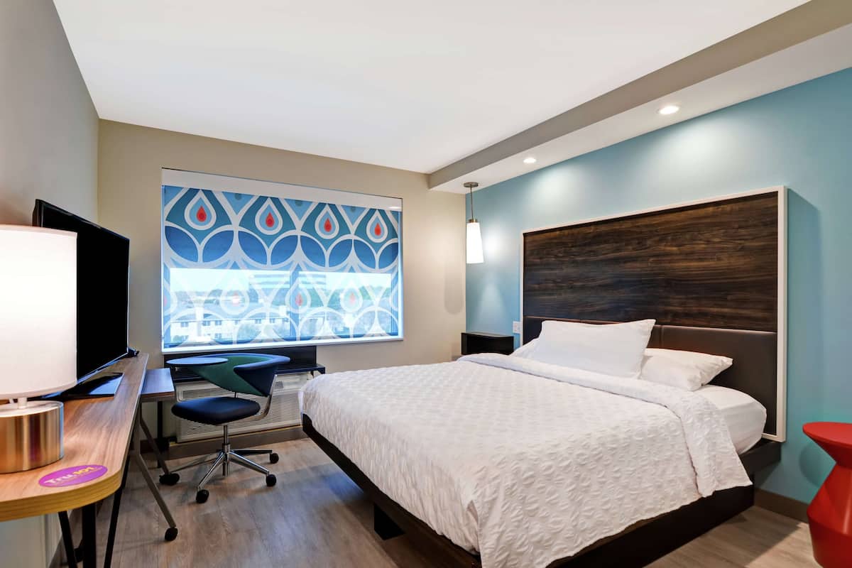 A modern hotel room with a large bed, a desk with a computer, a chair, and a TV.
