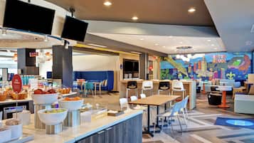 A modern hotel lobby with a buffet area, seating arrangements, and a mural depicting a cityscape.