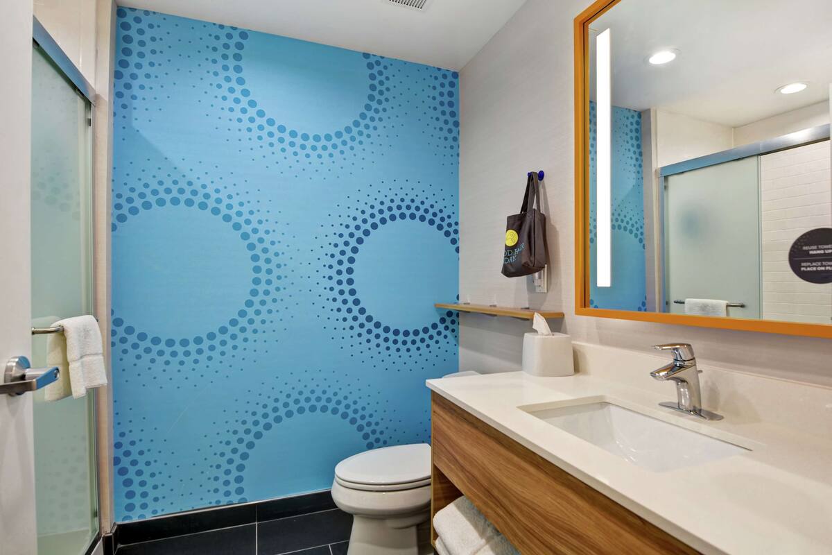 A modern bathroom with a blue patterned wall, a white toilet, a wooden vanity, and a mirror with a sign.