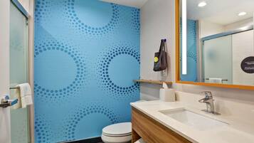 A modern bathroom with a blue patterned wall, a white toilet, a wooden vanity, and a mirror with a sign.