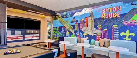 A pool table area with a vibrant mural of New Orleans, including the name 'BATON ROUGE'.