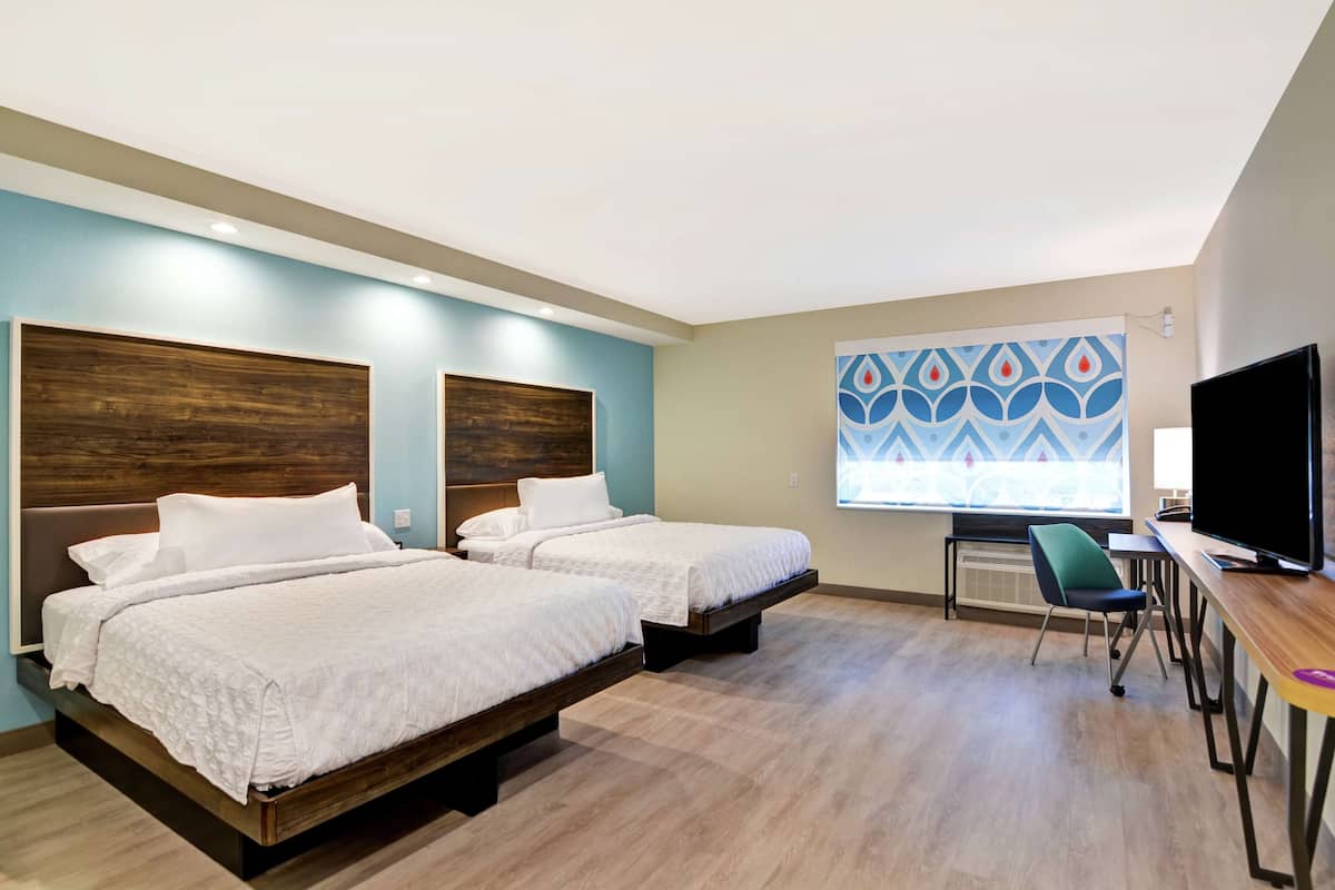 A hotel room with two beds, a desk, a chair, and a TV.