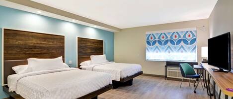 A hotel room with two beds, a desk, a chair, and a TV.