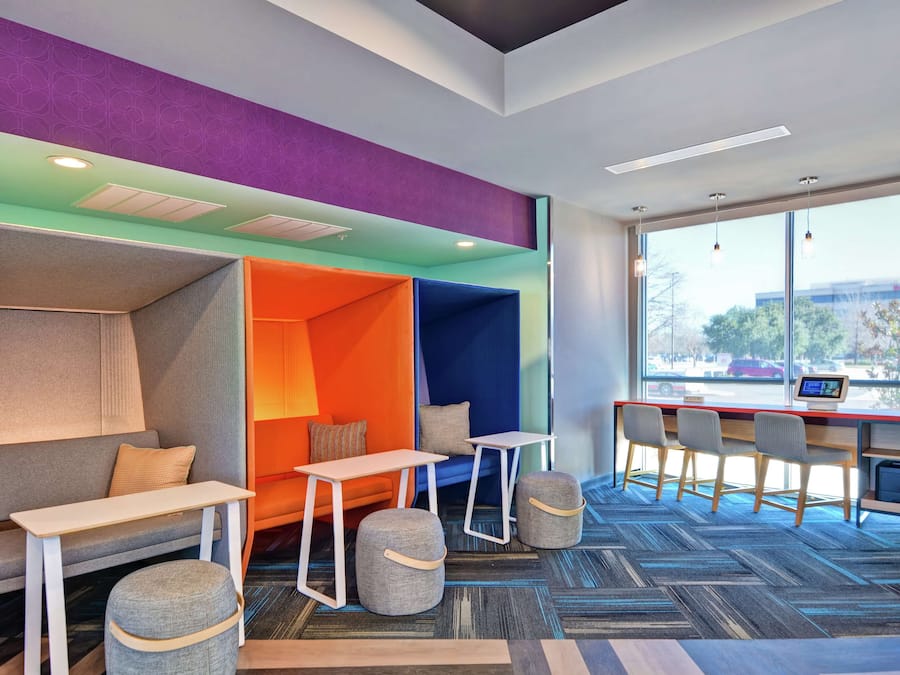 Un ufficio moderno con interni colorati, che include una zona relax con divano e pouf, una scrivania con sedie e un'ampia finestra con vista sull'esterno.