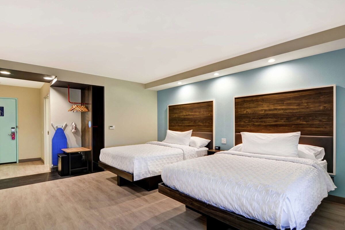 Une chambre d’hôtel avec deux lits, une tête de lit en bois, un mur d’accent bleu et un petit coin salon avec une table et des chaises.