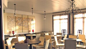 A spacious dining area with multiple round tables and chairs, a chandelier, and artwork on the walls. - Nastou View Hotel (Sintiki)