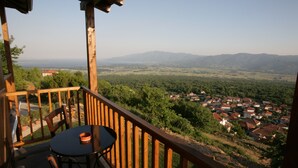 A wooden deck with a table and chairs, overlooking a village and mountains. - Nastou View Hotel (Sintiki)