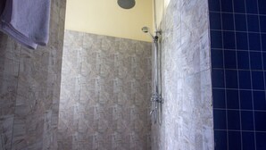 A shower with a handheld showerhead, a wall-mounted faucet, and a tiled floor. - Purnama Guest House (Ubud)