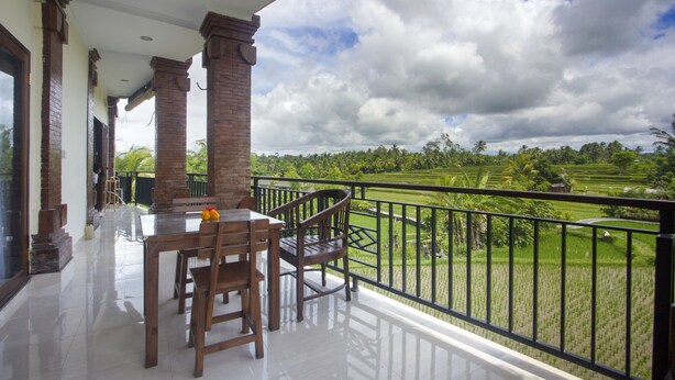 A balcony with a view of a green landscape, a table with chairs, and a railing. - Purnama Guest House (Ubud)