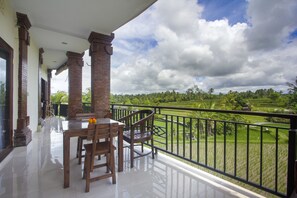 A balcony with a view of a green landscape, a table with chairs, and a railing. - Purnama Guest House (Ubud)