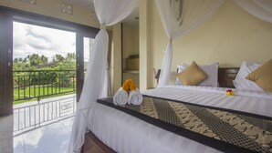 A bedroom with a large bed, white bedding, and a balcony with a view of greenery. - Purnama Guest House (Ubud)