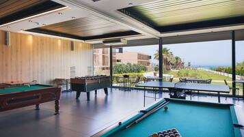 Zona de piscina con mesa de fútbol, mesa de billar y bolas de billar, con vistas a un jardín ajardinado y edificios.