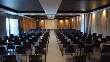 Ein Konferenzraum mit Reihen schwarzer Stühle, einer Projektionsleinwand und Holzwandverkleidung.