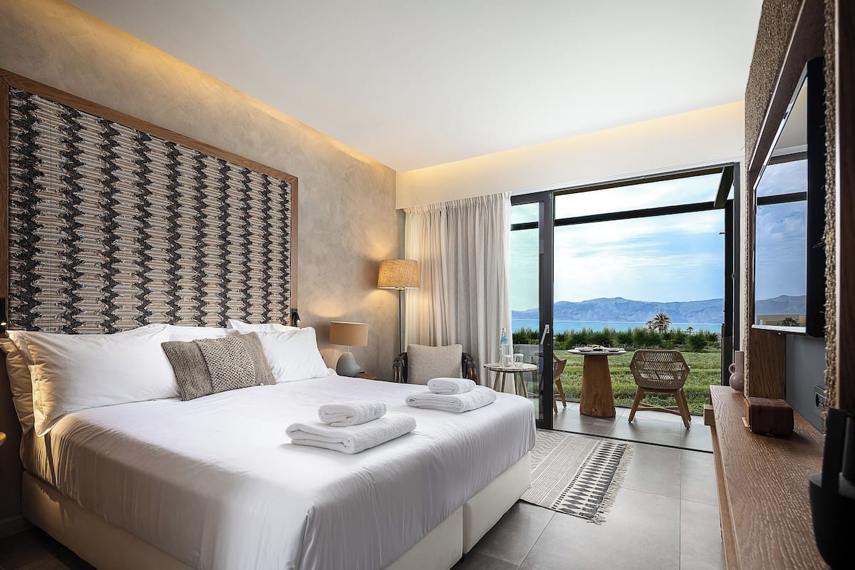 Ein modernes Hotelzimmer mit einem großen Bett, Blick ins Freie und einer kleinen Sitzecke.