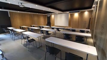A conference room with white tables and black chairs, a large screen, and wooden panel walls.