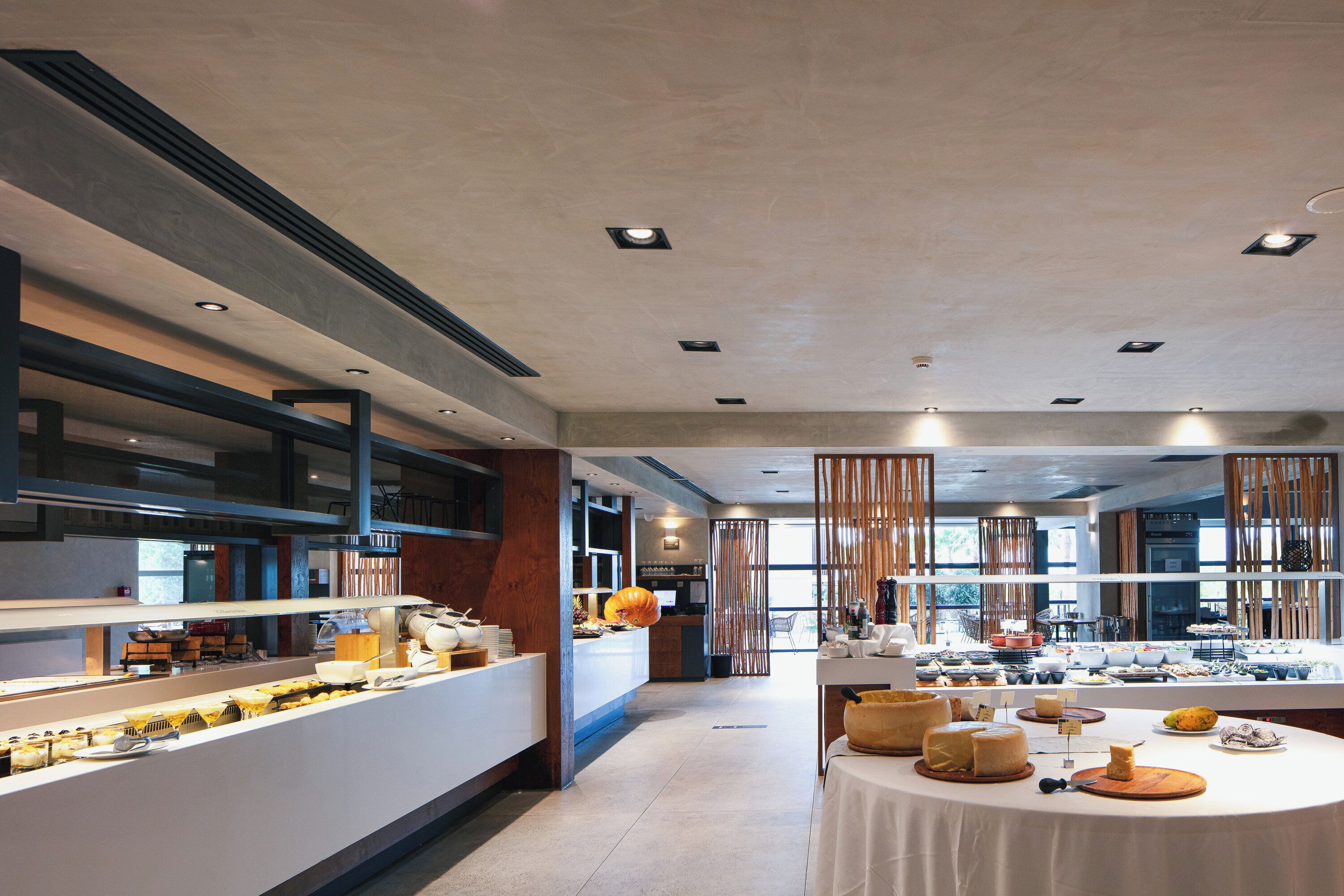 A modern hotel dining area with a buffet setup, a long counter, and a view of the kitchen in the background.