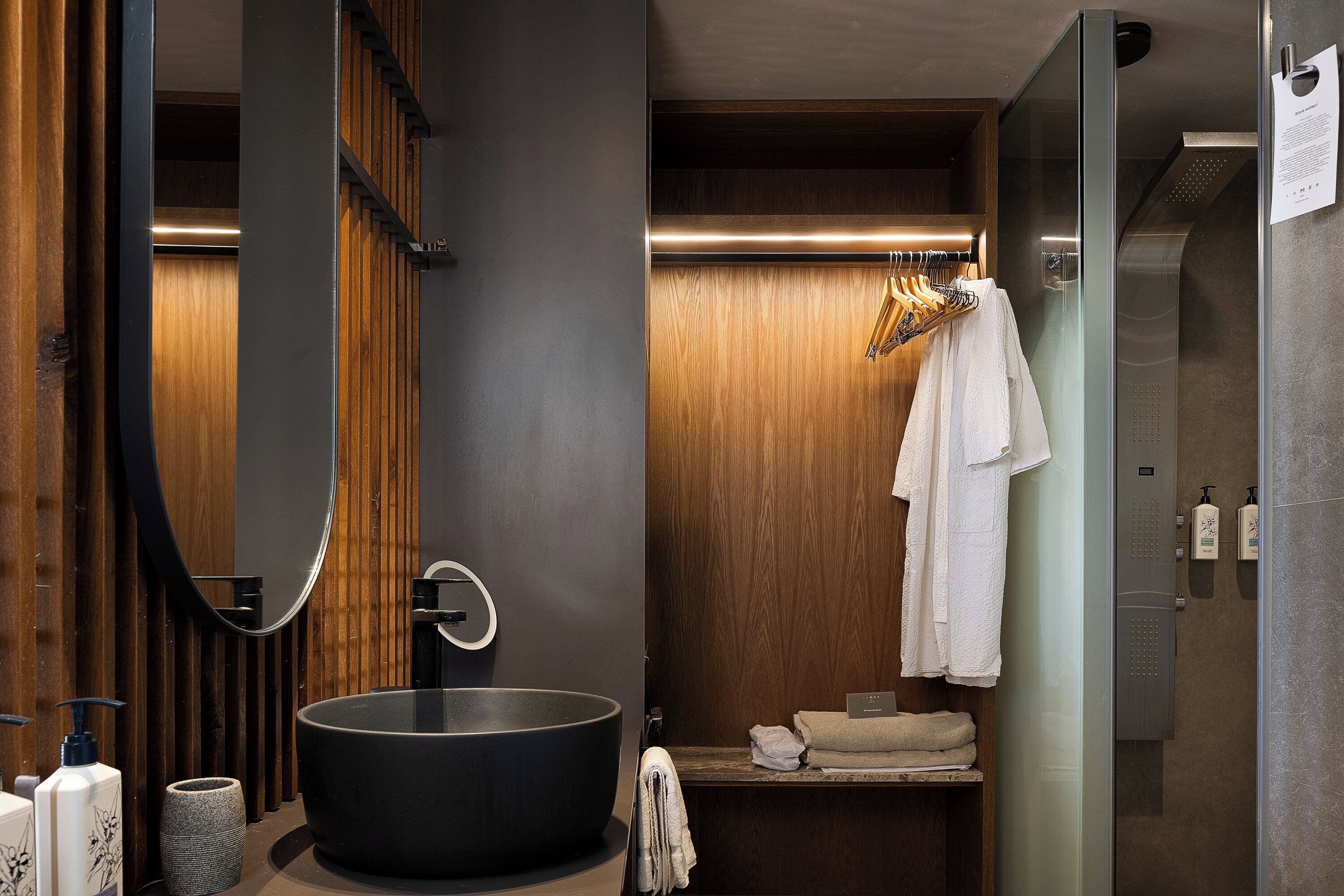 A modern bathroom with a large black sink, wooden paneling, a mirror, and a towel rack.