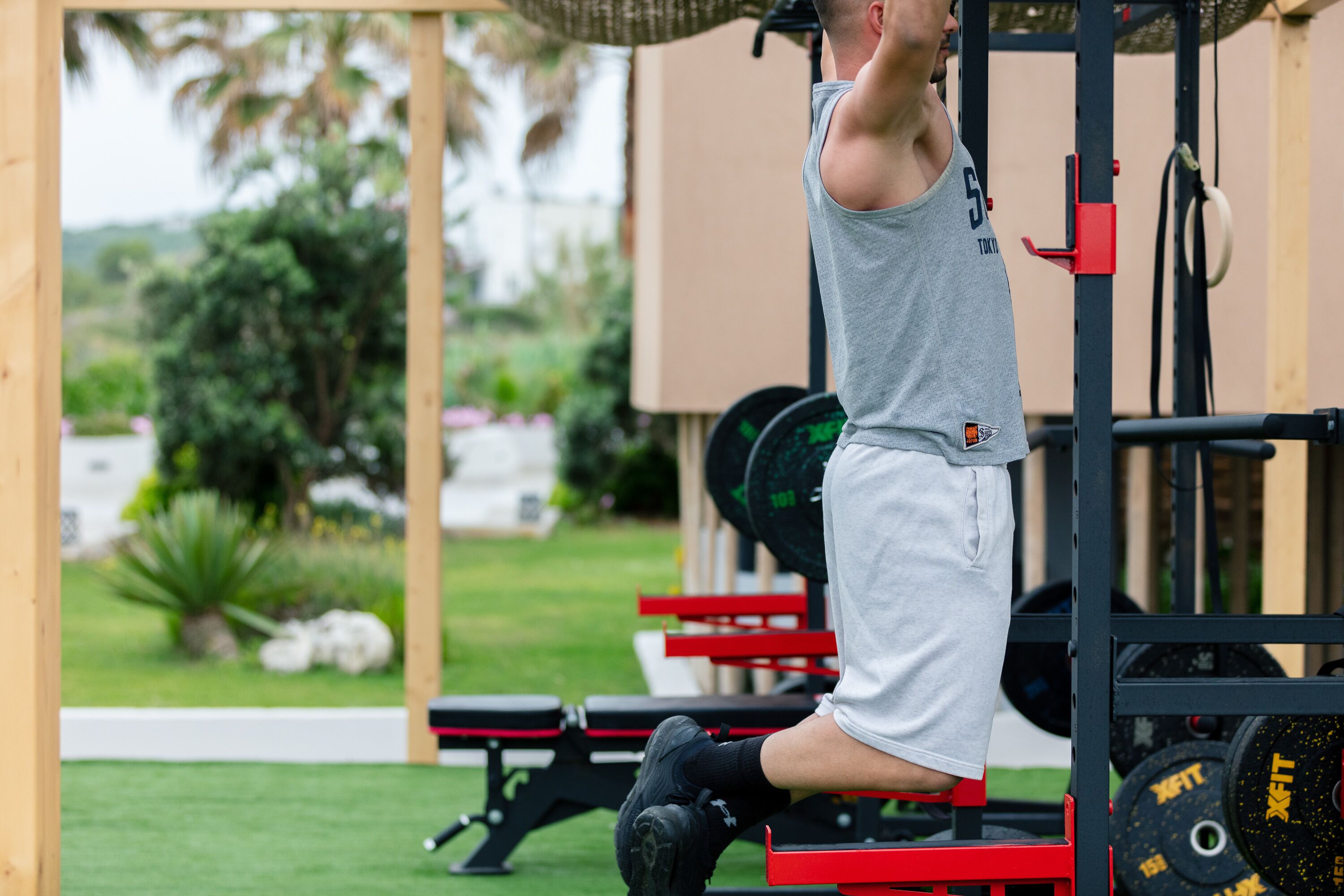 A person performing a pull-up exercise on a red bench under a black and red weightlifting station.