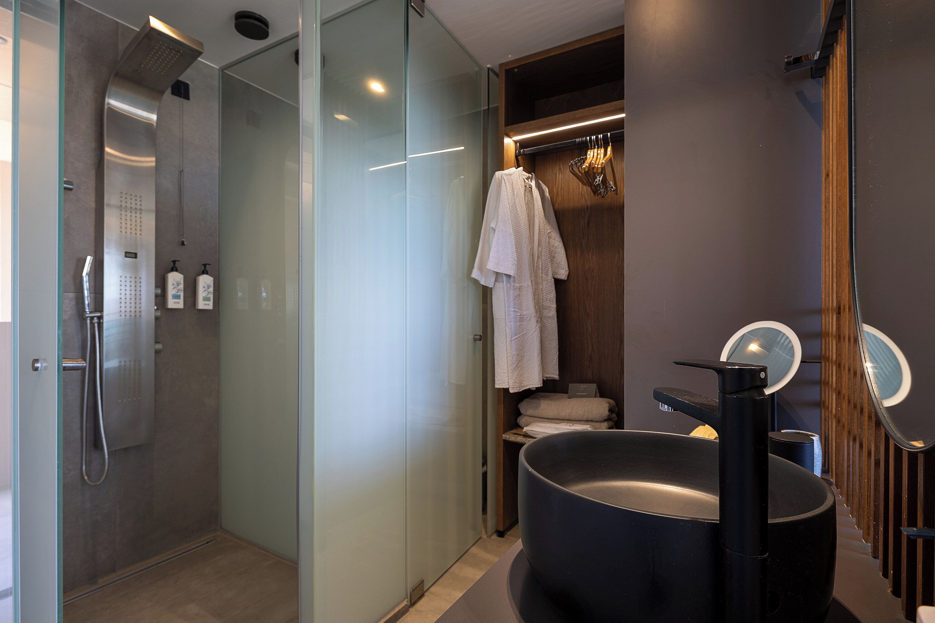 A modern bathroom with a glass shower enclosure, a large black sink, and a wooden vanity with a mirror.