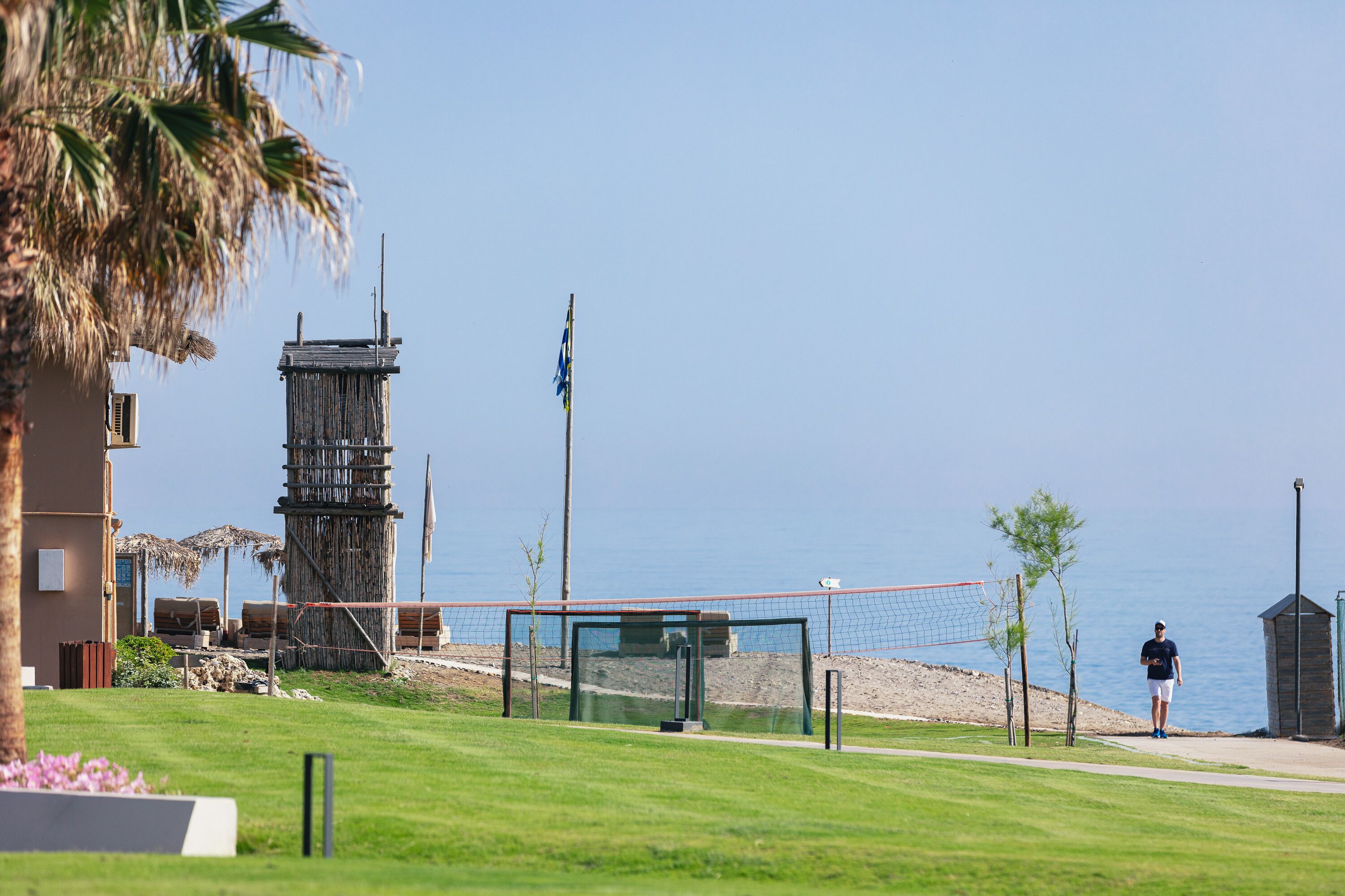 A beach volleyball court with a net, palm trees, and a building in the background.